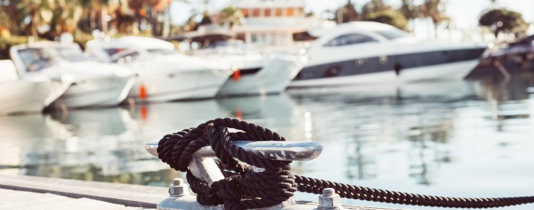 Mooring yacht rope with a knotted end tied around a cleat on a wooden pier against marina view